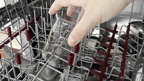 Close up of a female hand empty out the clean glass cups from a dishwasher rack