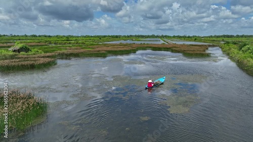 Aerial view of a peaceful waterway winding through flooded wetlands and rural farmland in An Giang, Mekong Delta, during the seasonal monsoon.