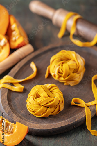 Homemade uncooked pumpkin tagliatelle or fettuccine noodles on a wooden board