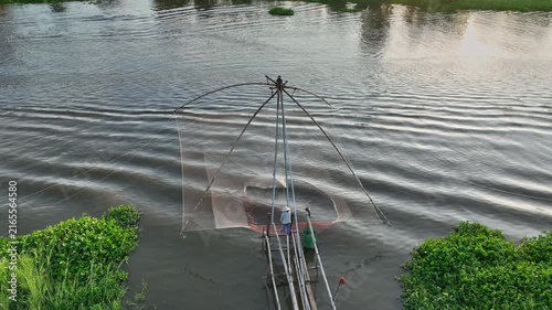 Aerial view of a fisherman using a traditional lift net from a narrow boat during the annual flood season in An Giang, Mekong Delta, Vietnam.
