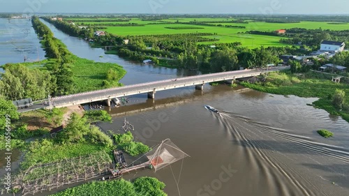 Drone view of An Giang in Vietnam's Mekong Delta during flood season, showing a bridge, boat wake, waterways, rice fields, rural homes, and a traditional fishing net.