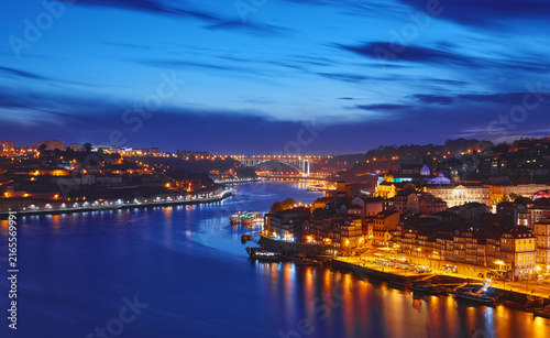 Porto, Portugal. Evening sunset panoramic view at nighttime town and Ponte de Dom Luis bridge with tramways. Coastline of river Douro with reflections of illumination in water and picturesque clouds.