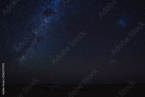 Cuadro en lienzo The Milky Way galaxy, Large Magellanic Cloud, Small Magellanic Cloud and constellations shine over a safari vehicle parked on the dark horizon in the desert landscape of Namibia