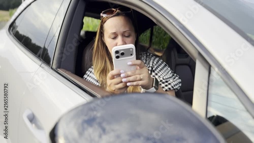 Young woman sitting in a car and covering her face while talking on a phone, looking stressed or upset
