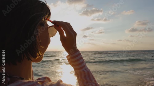  Young woman puts on sunglasses at sunset. Concept of a summer beach holiday. A sense of freedom and summer rest. Summer mood. Moment of happiness. 
