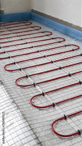 Red underfloor heating pipes installed on reinforcement mesh over thermal insulation layer. Radiant warm floor system construction and energy efficient home heating technology concept
