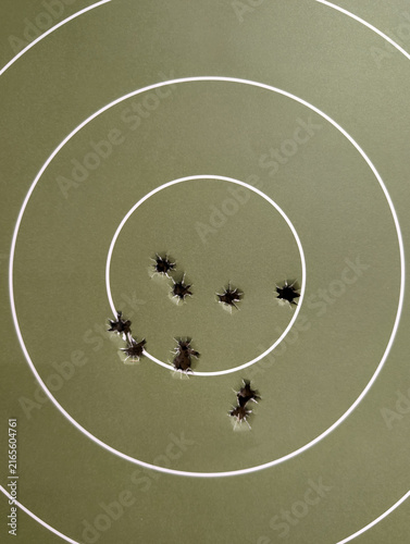 Принти на полотні Vertical close-up of a green paper target with a tight cluster of nine 9mm bullet holes from a pistol, demonstrating accurate marksmanship at a firing range