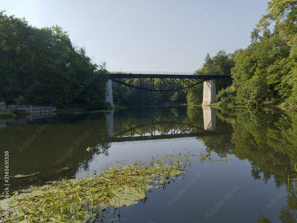 Naklejka premium Bridge over a river with trees on both sides and reflections in the water during a clear day