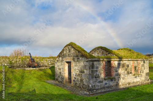 Fotografie The grass-roofed stone gunpowder magazine at Fort Eliza with a rainbow in the sky