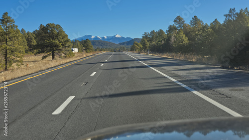 View from a moving vehicle on eastbound Interstate-40 approaching Flagstaff Arizona. The snow capped mountain in the distance is Humphrey's Peak.
