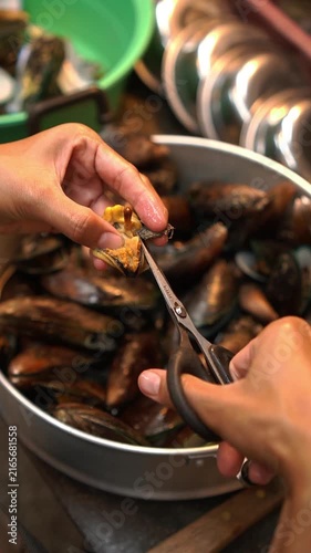Cooking Thai stir-fried mussels with sweet basil (Hoi Maelang Phoo Phad Ho Ra Pha). Sautéing chili and garlic, seasoning sauce, tossing with steamed mussels and basil.