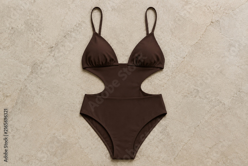 Minimalist monokini swimsuit laid flat on a textured stone surface.