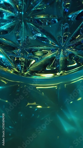Cut crystal glass casts turquoise and green caustic reflections across a dark glossy surface. Concept luxury optics for design, advertising, websites, banners, magazines and presentations.