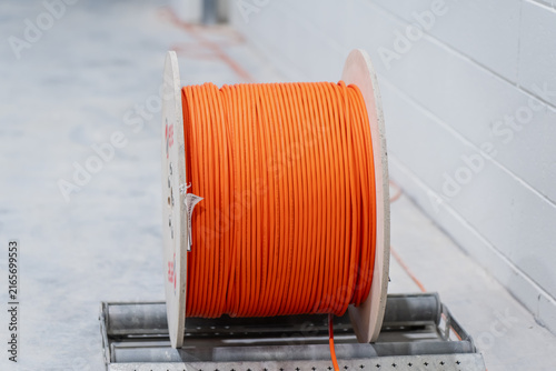 Large wooden spool loaded with orange telecommunication cable positioned on a metal roller dispenser during utility installation work