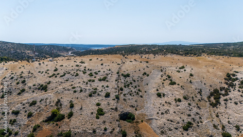 Aerial view of the rocky landscape of Rab island with sparse vegetation, a stone wall dividing the terrain, and distant sea views in Rab, Primorje-Gorski Kotar, Croatia.