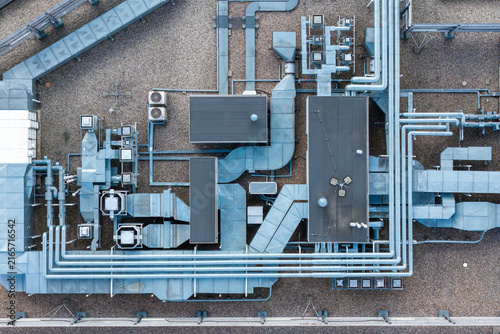 Aerial view of the roof of a self sufficient office building featuring complex ventilation ducts, HVAC units, and metallic piping arranged on a gravel surface in Poland.