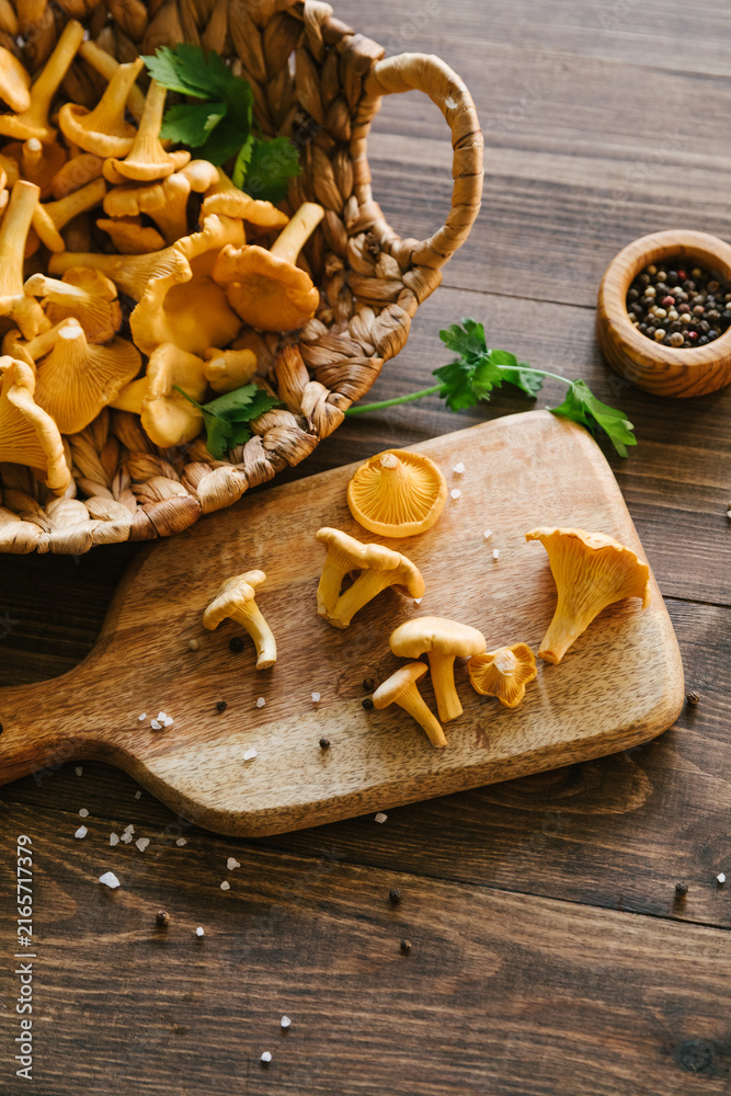 Fototapeta premium Fresh chanterelle mushrooms in a wicker basket and on a wooden cutting board in a rustic kitchen, gourmet cooking ingredients, healthy harvest, autumn food scene.