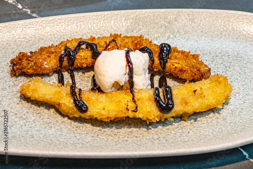  Professional chef hands plating a gourmet grilled banana dessert with vanilla ice cream and rich chocolate sauce.