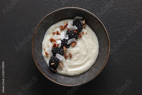 Fotografie Semolina milk porridge or pudding with berries and nuts in a bowl on the table