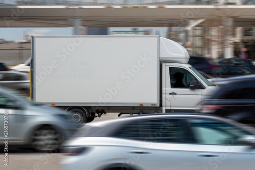 White delivery van in focus driving through heavy traffic with blurred cars in speed around it. Copy space on the cargo hold.