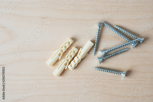 Plastic wall anchors and metal screws on wooden background