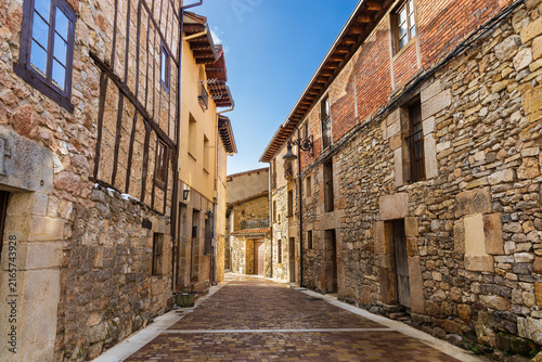 Narrow deserted alley with Castilian stone houses bathed in bright sunlight. Aguilar de Campoo, Palencia, Castile and Leon, Spain.