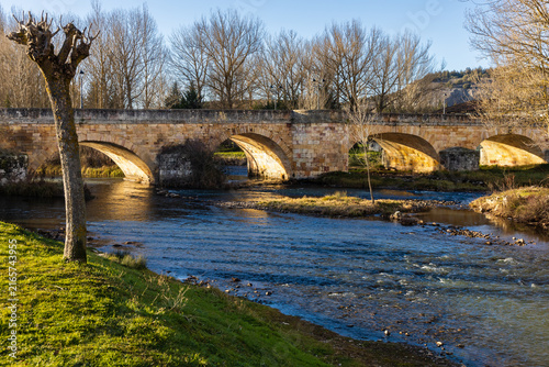 Pisuerga River and traditional medieval stone arch bridge on a mild winter day. Aguilar de Campoo, Palencia, Castile and Leon, Spain.