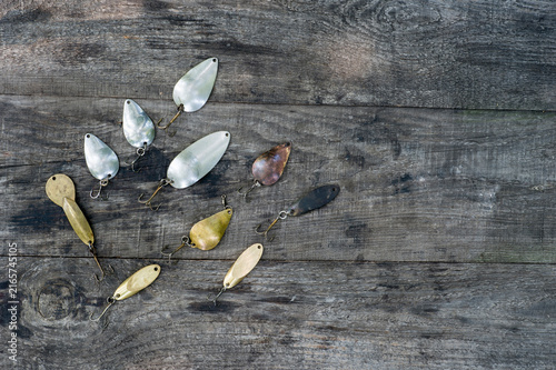 Metal spinners in the shape of a spoon of different colors for catching a predator on a vintage wooden background.