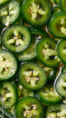 topdown view of sliced green jalapeno peppers in brine, vibrant green pickled jalapeno slices with visible seeds, preserved jalapeno pepper rings submerged in brine
