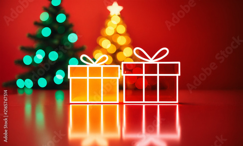 two glowing neon gift boxes with bright outlines on a shiny red reflective surface in front of out of focus illuminated christmas trees and bokeh lights.