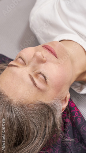 Woman resting upside down with closed eyes on mat with scarf expressing calmness and wellness relaxation concept