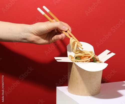 Woman eating tasty takeaway wok with chopsticks at white table on red background  closeup