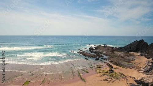 Dramatic aerial view of the atlantic ocean waves washing over the unique rock formations and sandy beaches of costa vicentina near aljezur in algarve, portugal, on a bright sunny day