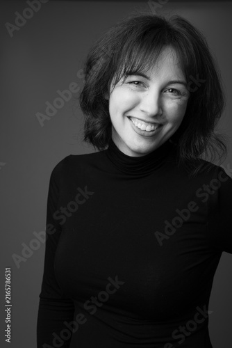 Fotografía Black and white studio portrait of a smiling 39-year-old woman with dark hair wearing a black turtleneck against a simple gray background