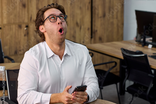 Fotografie Young businessman in office reacting with surprised expression while looking upw
