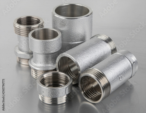 close-up view of various stainless steel threaded pipe connectors, adapters, and metal coupling fittings arranged on a reflective industrial surface