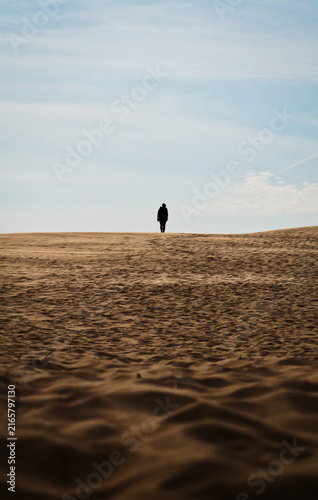 Foto Lone silhouette walking on sand dune against clear sky