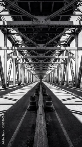 Symmetrical black and white perspective looking down the center divider of a massive steel truss bridge