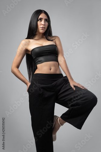 Attractive young Latina woman wearing a black top and pants poses confidently in a professional studio, highlighting fashion, beauty, elegance and modern style