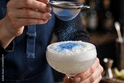 Bartender sifting blue matcha powder over foamy cocktail foam