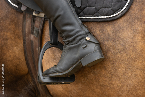 Close up of a horse rider with their foot in the stirrup with their toes pointing down and heels up. Horse riding foot position. Equestrian riding heel squeezing horse forward. 