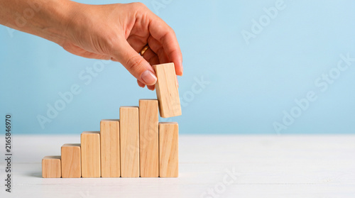 Hand placing wooden block on growing business growth tower against blue sky background