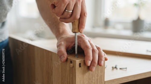 Close-up on hands assembling a wooden furniture with a screwdriver, highlighting the meticulous process of construction and DIY.