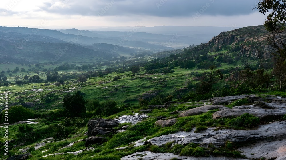 Fototapeta premium A lush green valley with rocky terrain and rolling hills under a cloudy sky offering a serene natural landscape