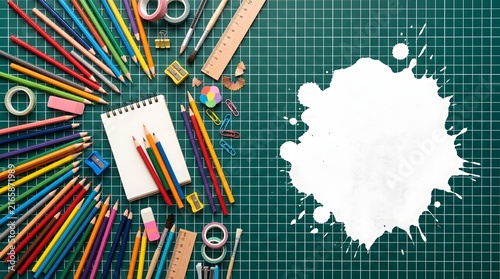 Colorful pencils and stationery on a green cutting mat with a white paint splash frame