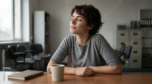 Woman with short dark hair sitting at her desk with eyes closed taking a slow breath during a work break