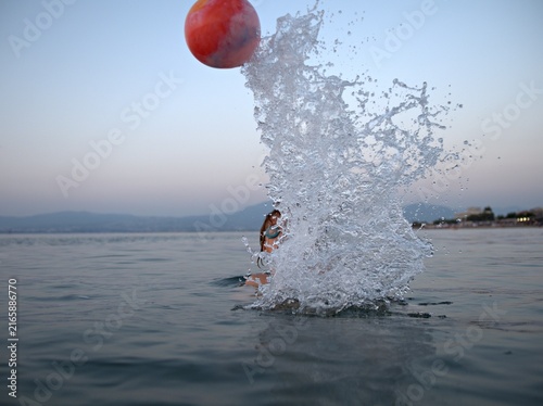 Fotografie Red ball flies up out of a burst of spray in the calm sea, the water lit by the