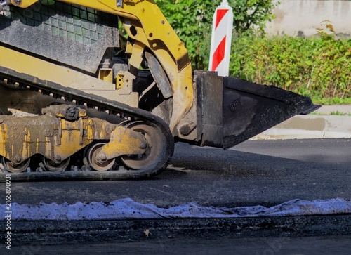 Bild auf Leinwand Yellow compact track loader with muddy tracks on an asphalt road during street c