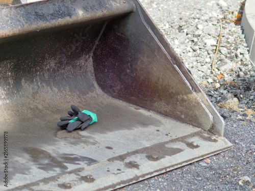 Фотография Black work gloves resting inside a dirty excavator bucket on a construction site