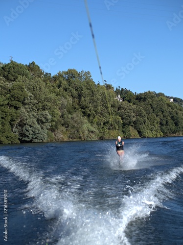 Obraz na płótnie Water skier follows the boat down the middle of a river below steep wooded slope
